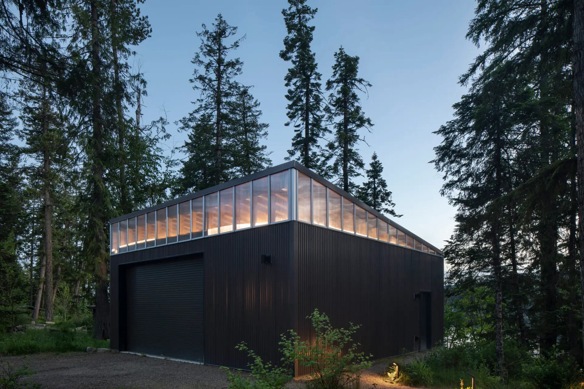 Priest Lake Cabin detached garage with dark siding and upper clerestory windows made of polycarbonate.