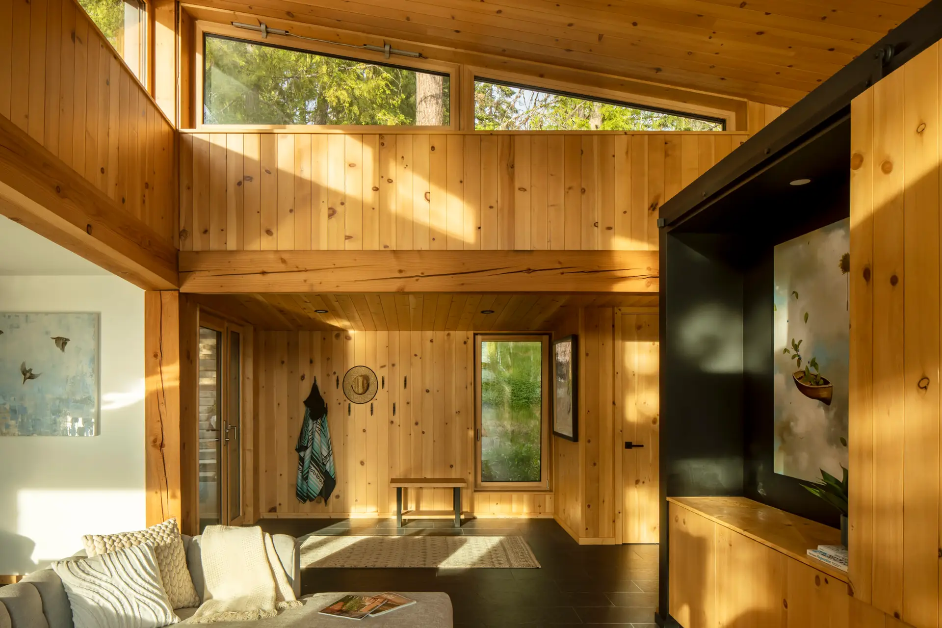 Priest Lake Cabin living room, featuring all wood walls and an upper clerestory window that follows the gentle slope of the ceiling.