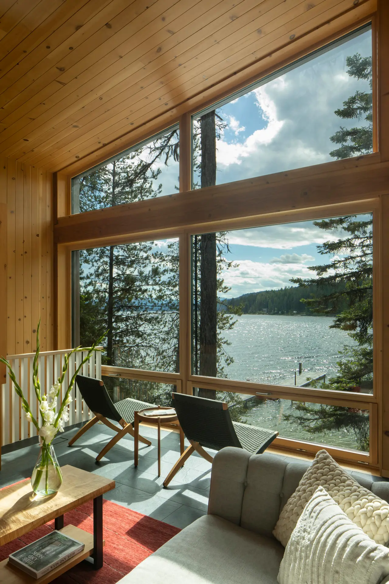 Priest Lake Cabin living room with a view out to the lake. The wall in the frame is a full window wall with a gently sloped wood ceiling.