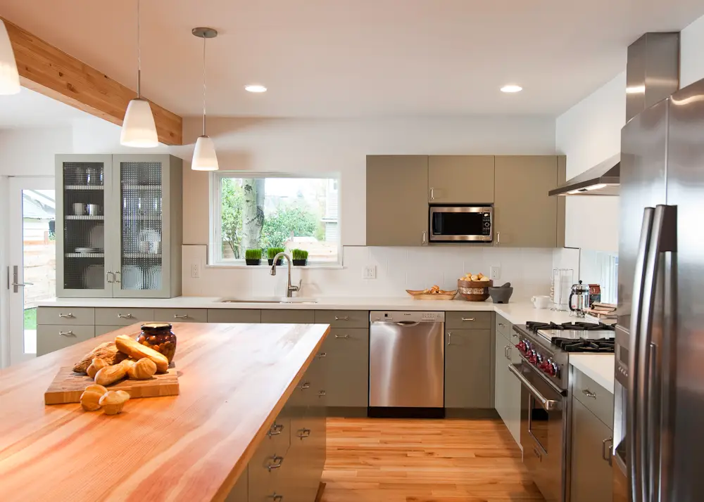 Kitchen of the Hale remodel with the island and kitchen sink as a focal point. THe custom cabinetry is in a muted sage green, paired with silver pulls and stainless steel applicances.