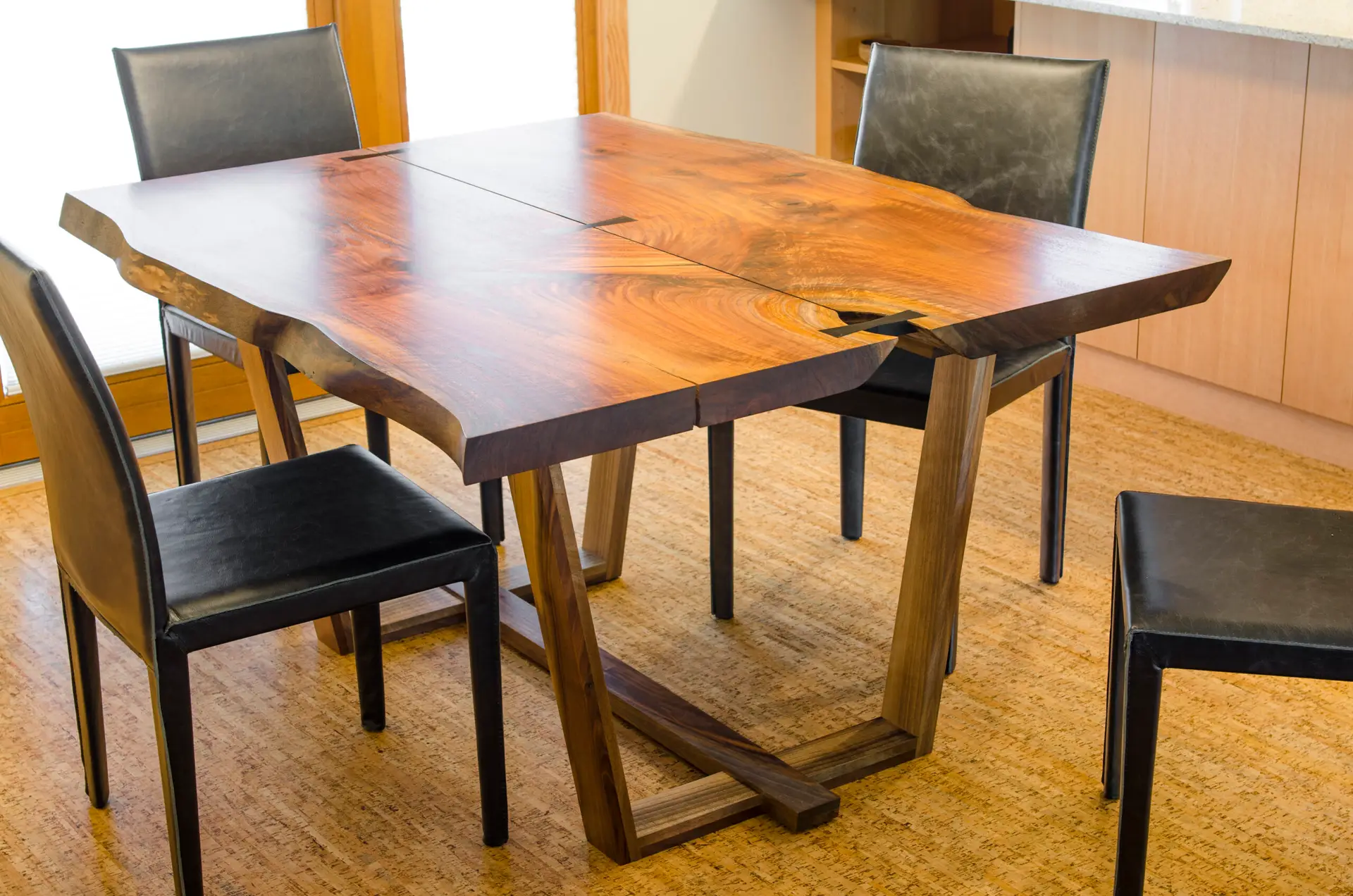 A custom live-edge dining table as part of the sustainable interior design at Ankeny Row, a net-zero energy community in Portland, Oregon. The table is crafted from bookmatched slabs of Oregon Black Walnut, a material known for its deep chocolate tones and striking grain. It features a "live edge," preserving the natural, organic contours of the tree. Several dark butterfly joints (or bowties) are visible across the surface. These are functional elements used to stabilize natural cracks in the wood while serving as a decorative "handcrafted" detail.
