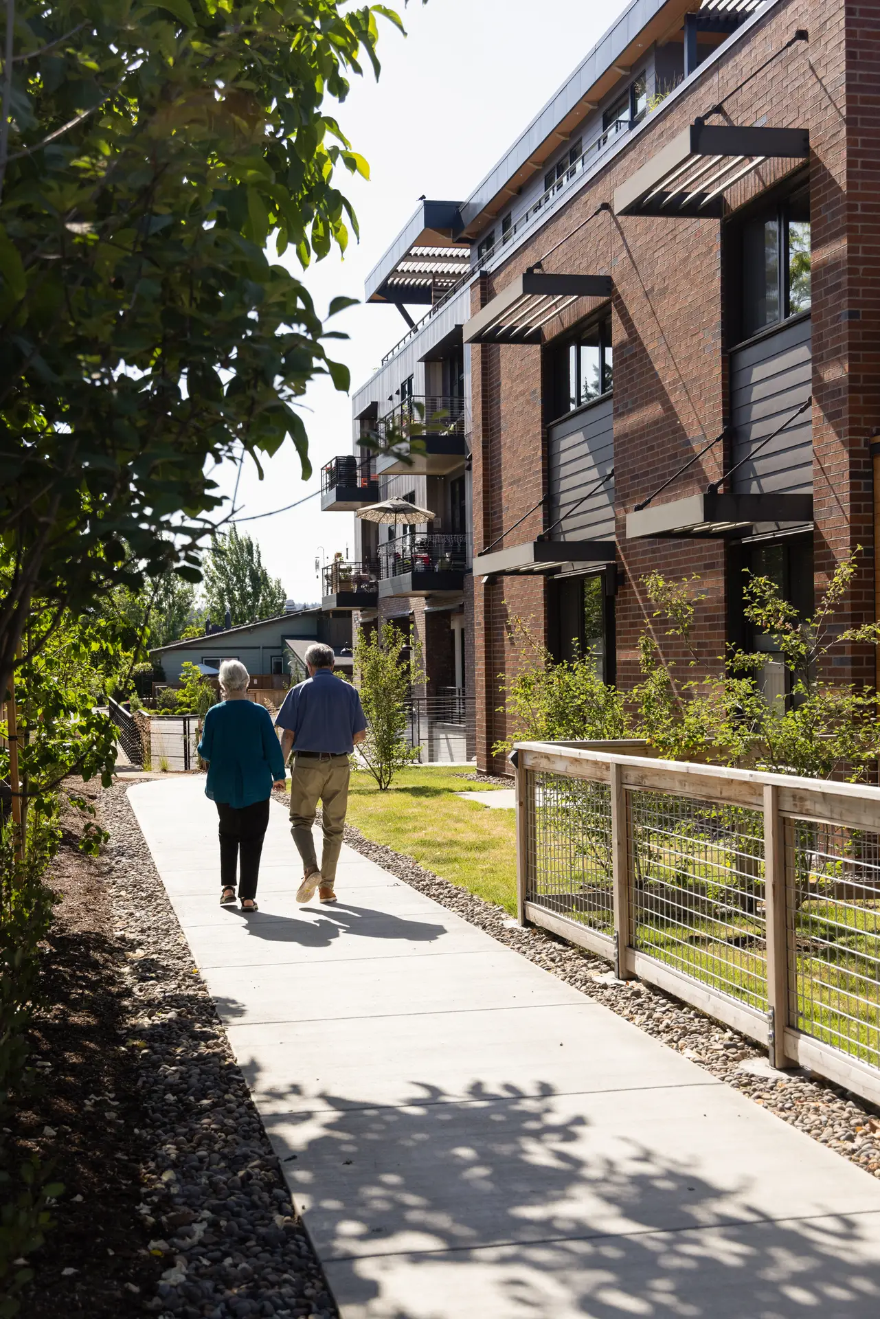 Trillium Townhomes at Rose Villa, looking down a walking path adjacent to the building. On the right the brick clad building with fixed solar shades above the south facing windows.