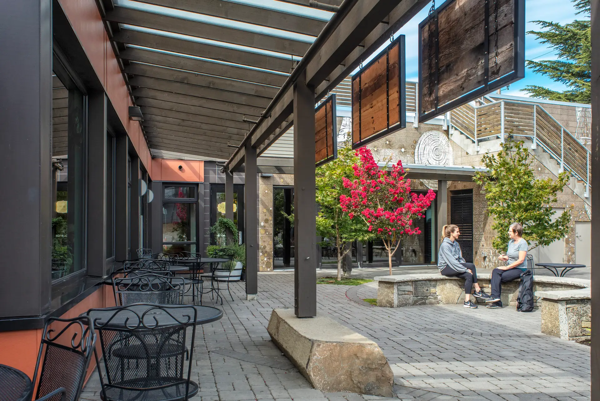 Courtyard at The Breath Building, featuring an awning and cafe tables. The columns of the awning come down onto an expressive stone that has a octagonal form --reminiscent of the regions columnar basalt formations.