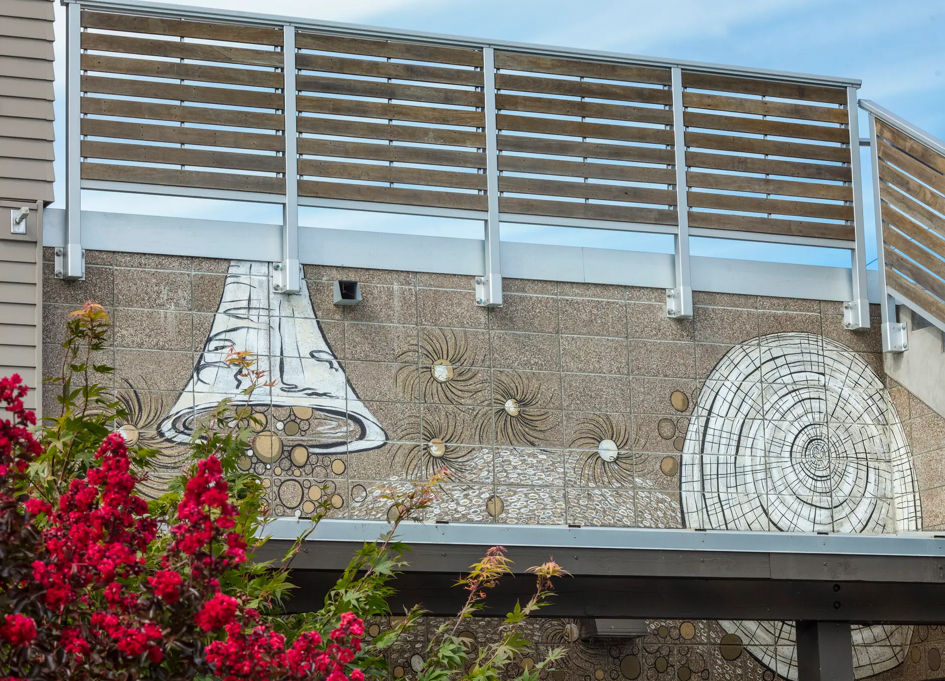 The Breath Building mural, which is a whimsical bell and tree design with careful linework and monochrome pallet. The frame contains flowering tree to the bottom left and the top of the image is showing the roof guardrails.