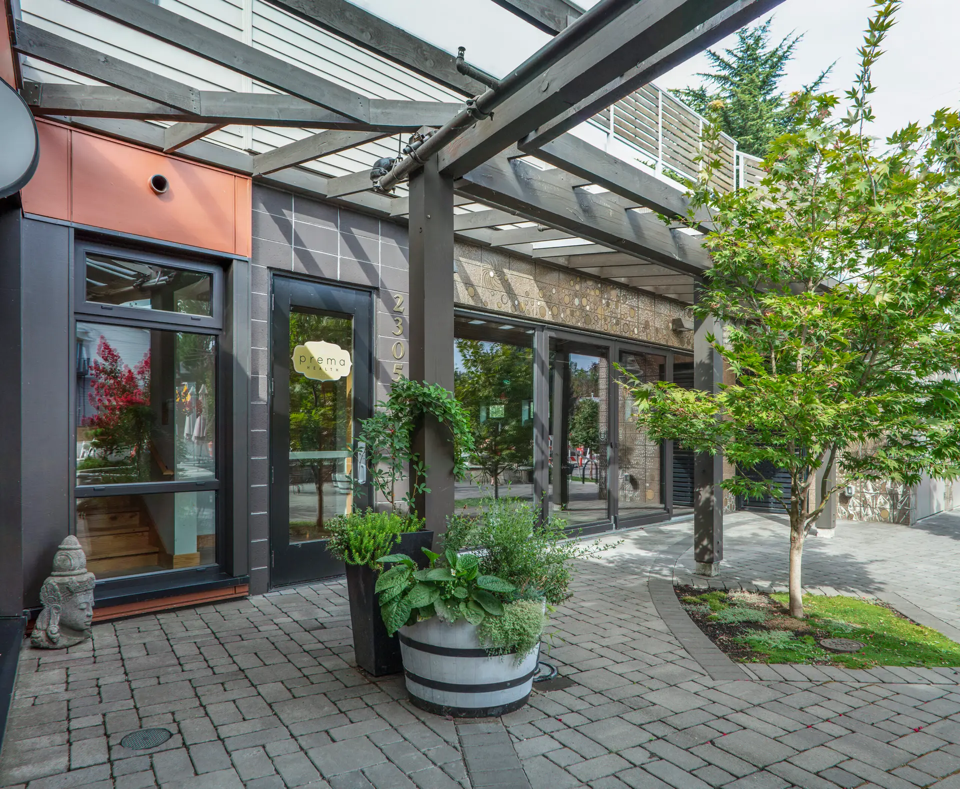 The Breath Building exterior, featuring a steel metal awning and planters. The walking surface material is a grey cobbled paver design.
