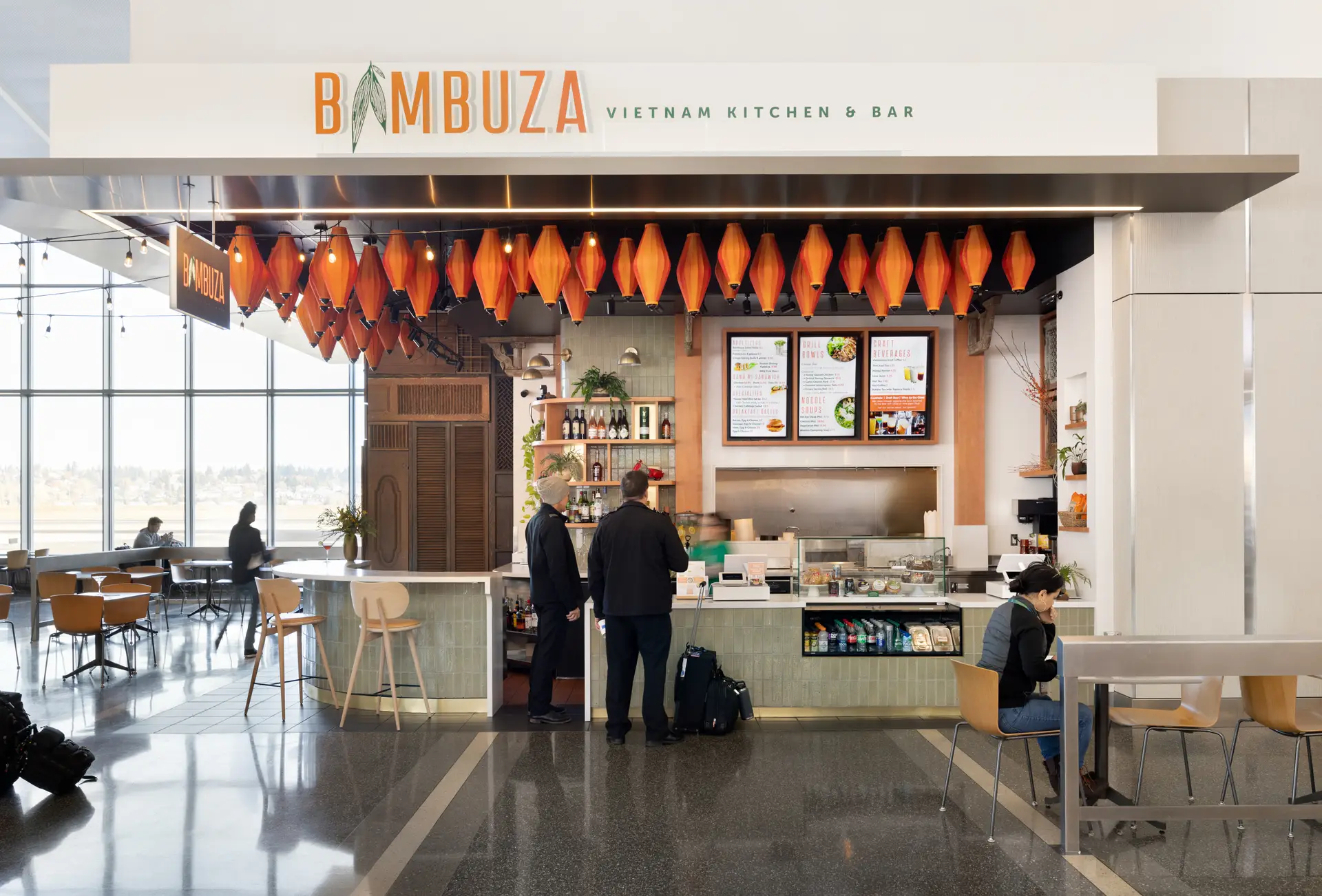 Customers ordering food at the counter at Bambuza. The signage is placed to the top of the frame and the ordering counter is indicated by beautiful orange lanterns above.