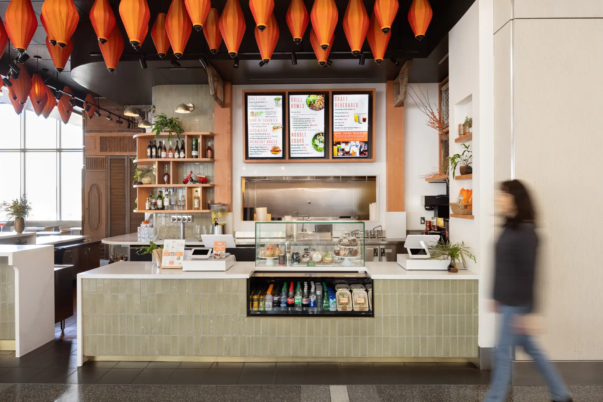 View of the counter at Bambuza, featuring beautiful orange lanterns and sage green tile on the face of the counter.