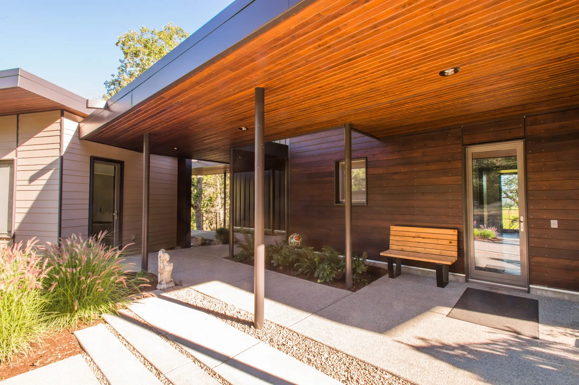 Cowhorn residence exterior patio featuring wood ceiling and carefully placed posts that help to define the planted garden spaces and walkway spaces.