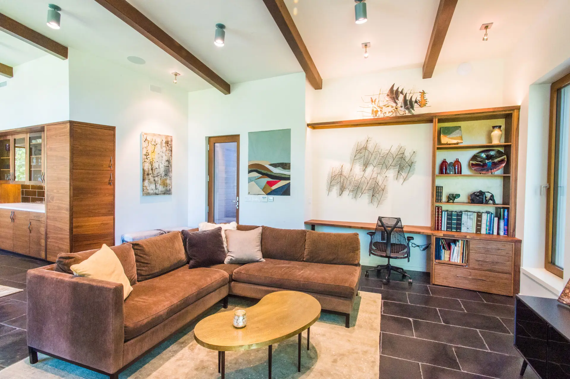 Cowhorn residence living room with dark tile floors, light white walls, exposed beams above, and several built in cabinets.