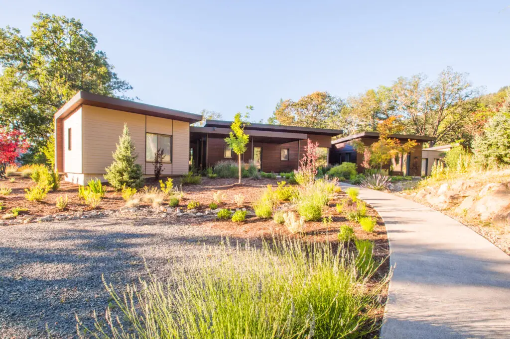 Cowhorn residence exterior view, featuring a gentle arcing pathway to the front door and landscaping along the way. The home features a low slope roof and a modern aesthetic.