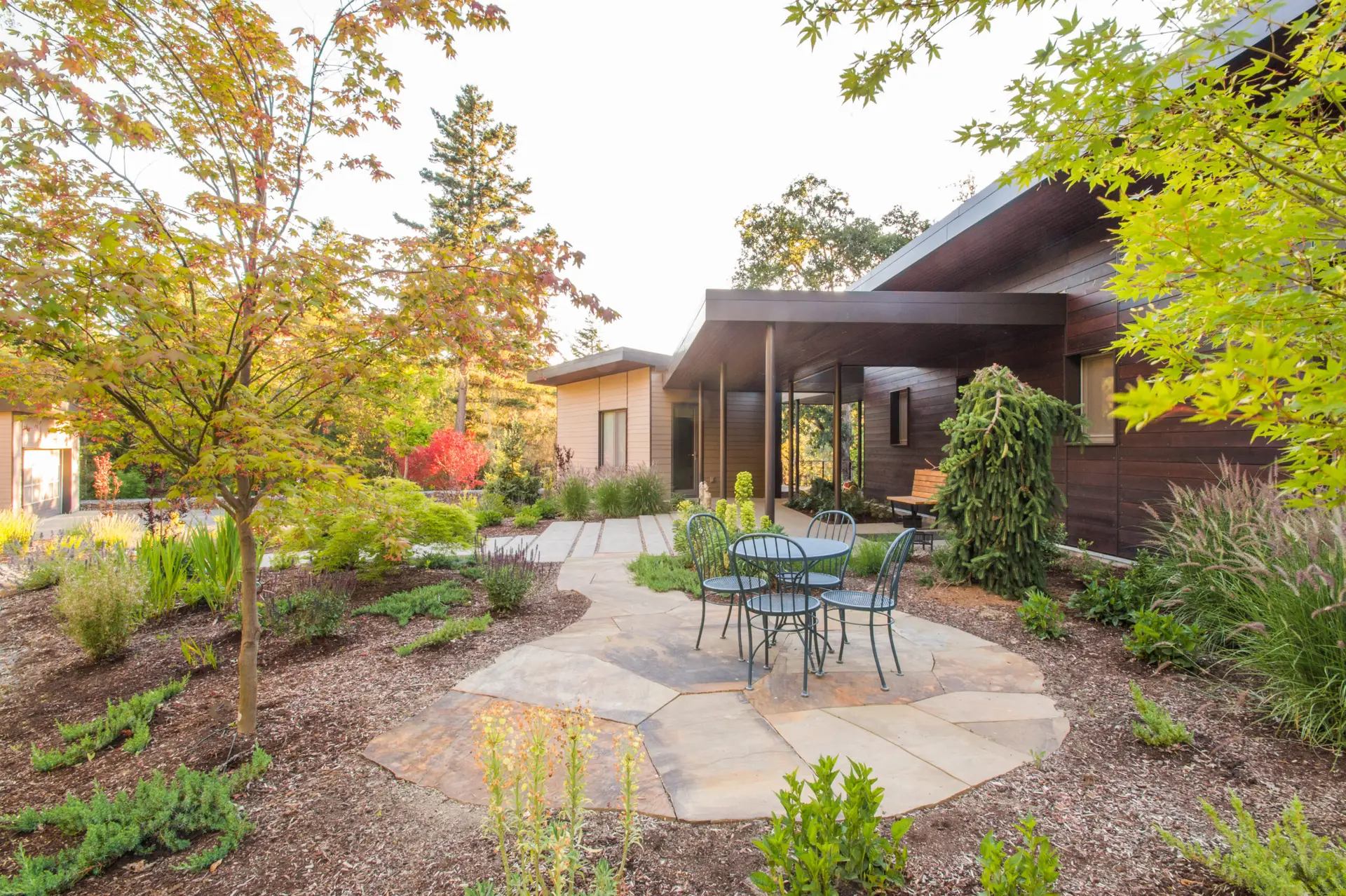 Cowhorn residence exterior patio space featuring large flagstone paving and a quaint patio set. Trees and low shrubs frame the view.