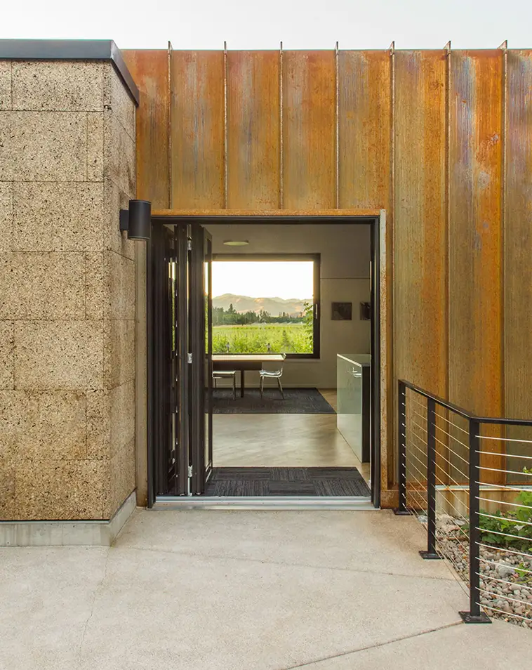 exterior entry view of Cowhorn, showing pre-oxidized metal panel and cork sizing. A view through the space and out toward the winery beyond can be seen through the entry.