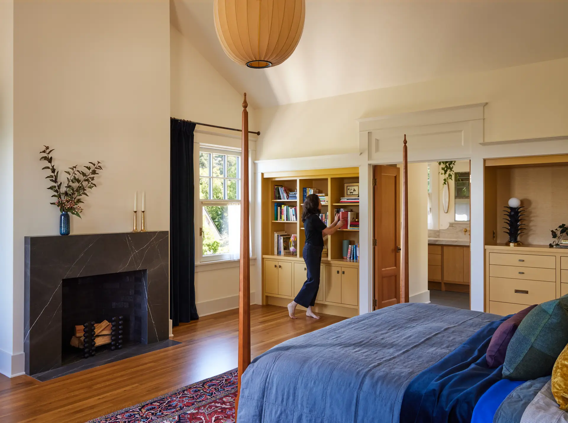 Willamette Heights House Bedroom, featuring a vaulted ceiling, built in shelving, a fireplace to the left of frame, and the primary bathroom beyond.
