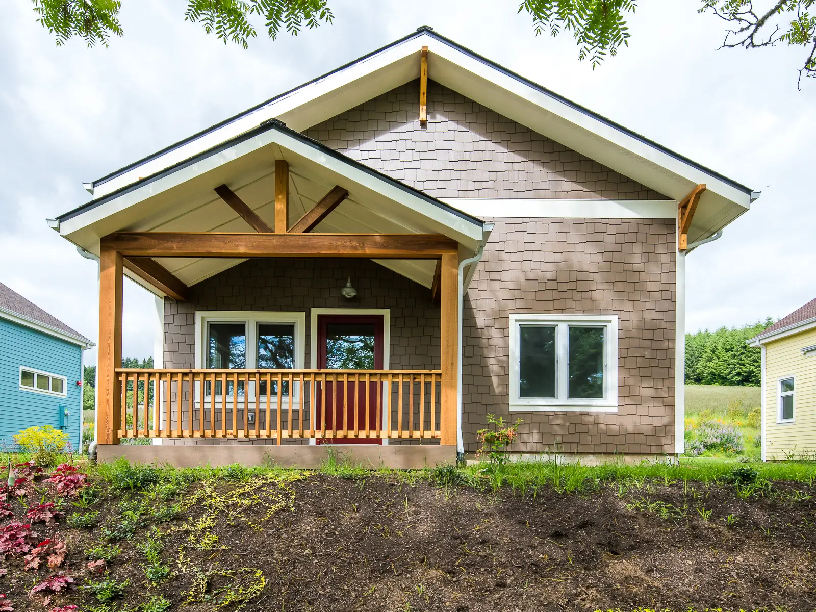 Green Grove CoHousing exterior view, showing a home that is a craftsman style brown home with white trim. There is an extruded gable that covers the front porch which is wood tone