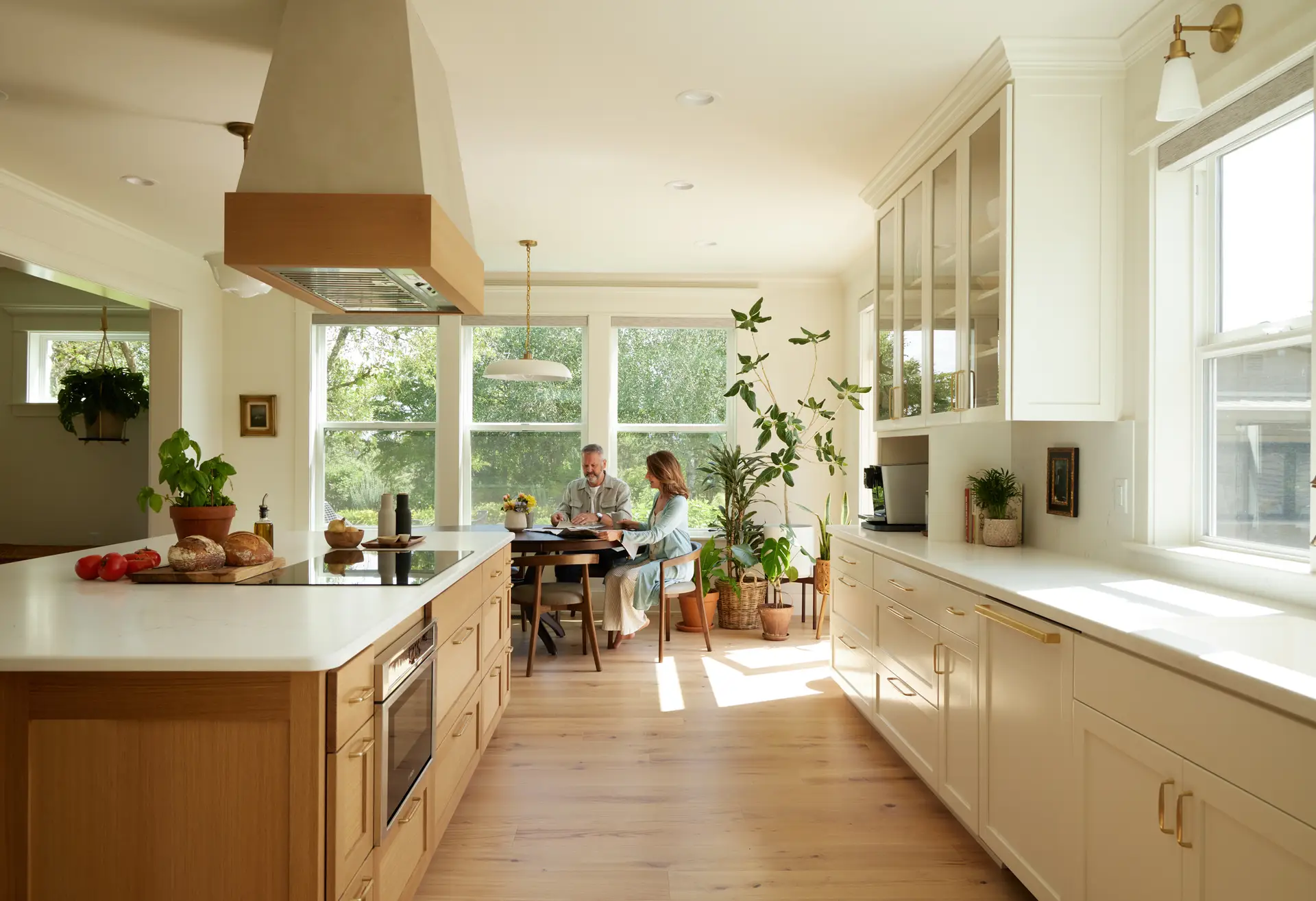 St. Paul Residence kitchen with the island to the left and a straight run of cabinets to the left. A couple can be seen in the dining room beyond with a window viewing outside in the back of the frame.