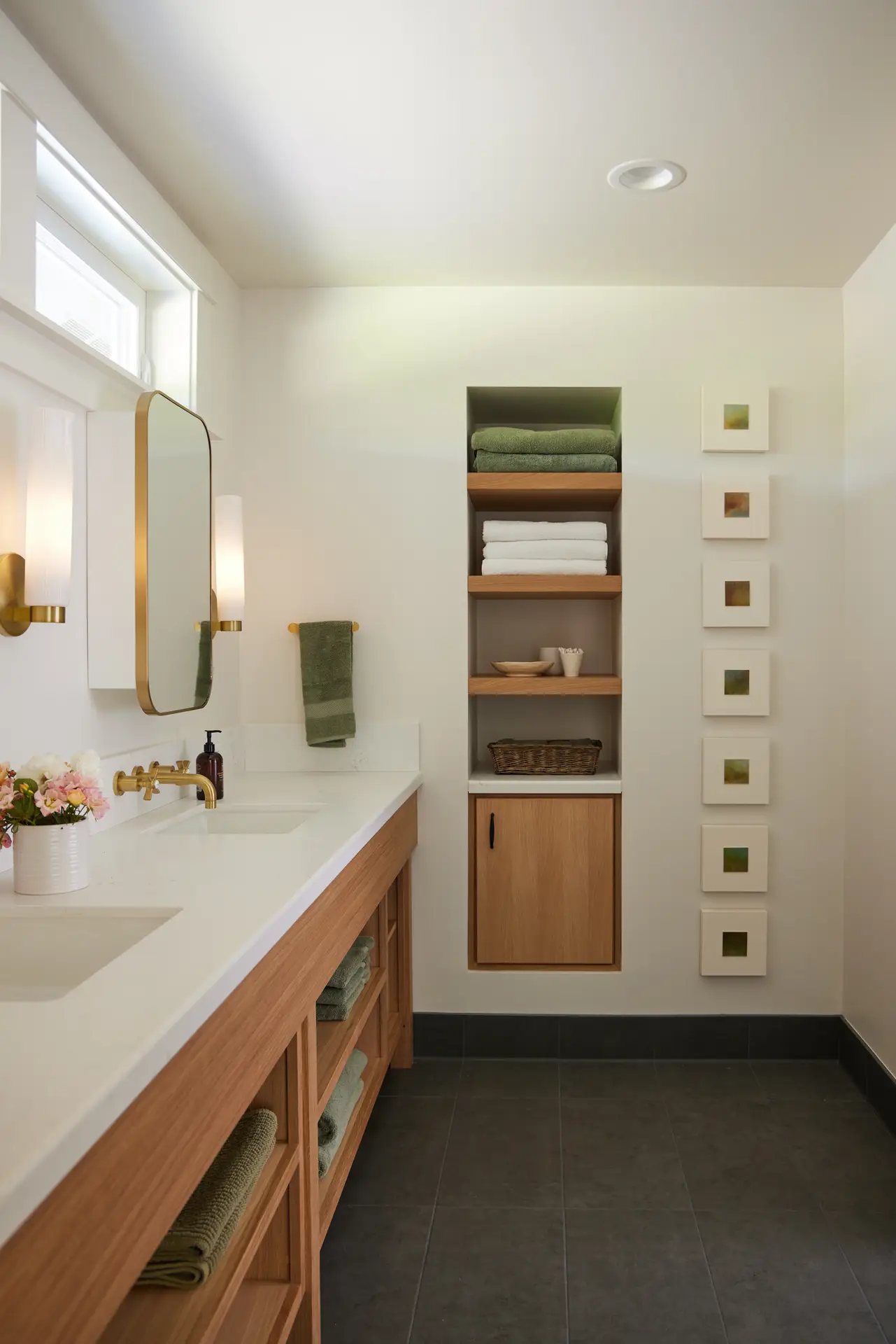 St. Paul Residence bathroom, featuring a dark tile floor, complimented by light walls and a clerestory window. A built in nook for bathroom linens and supplies is in the center of the frame.