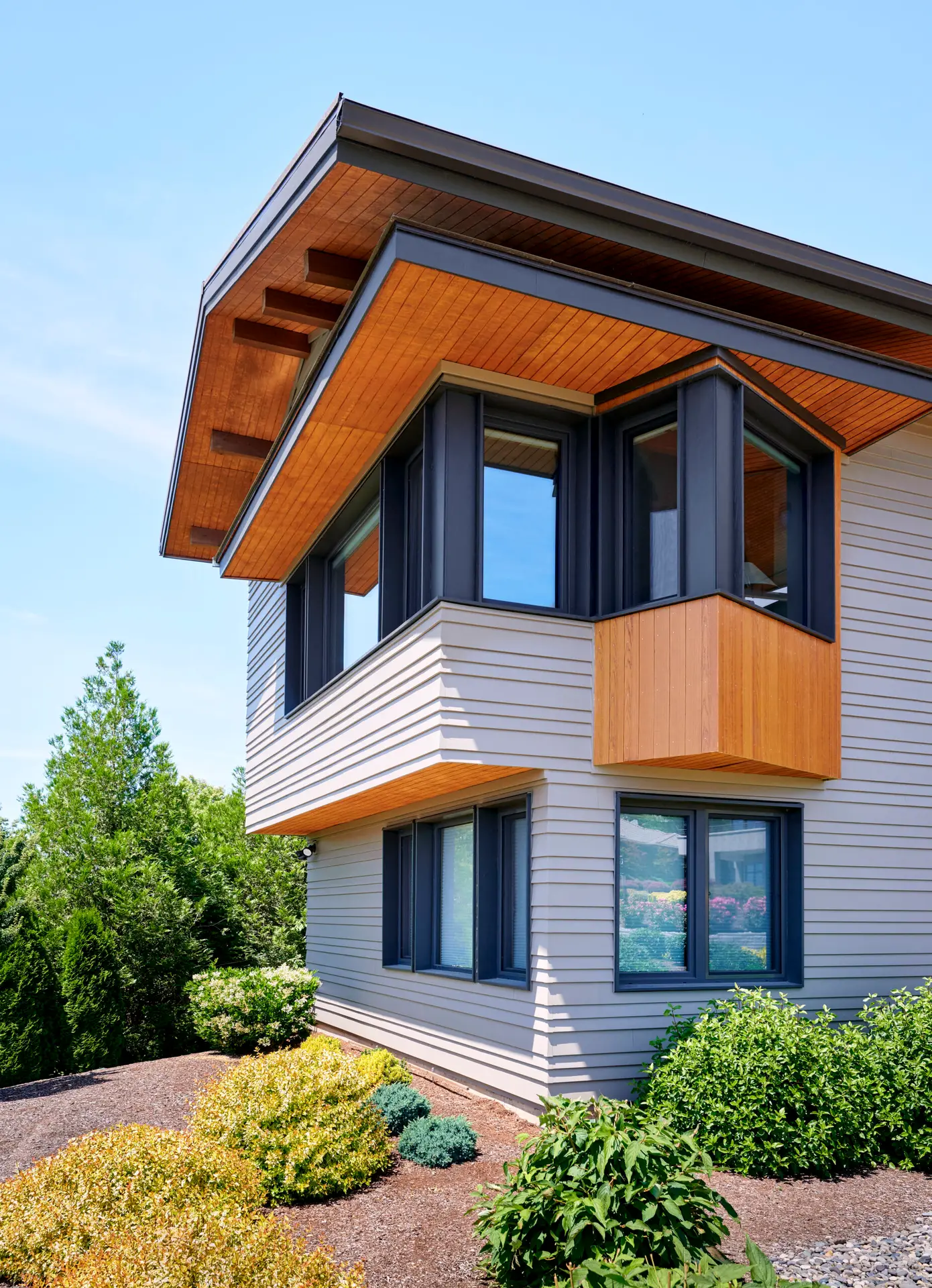 Vancouver Residence exterior, featuring light grey exterior fiber cement siding combined with a natural wood soffit and rotated angle bump out on the 2nd floor that is also clad with wood. The home features deep overhangs to help with shading.