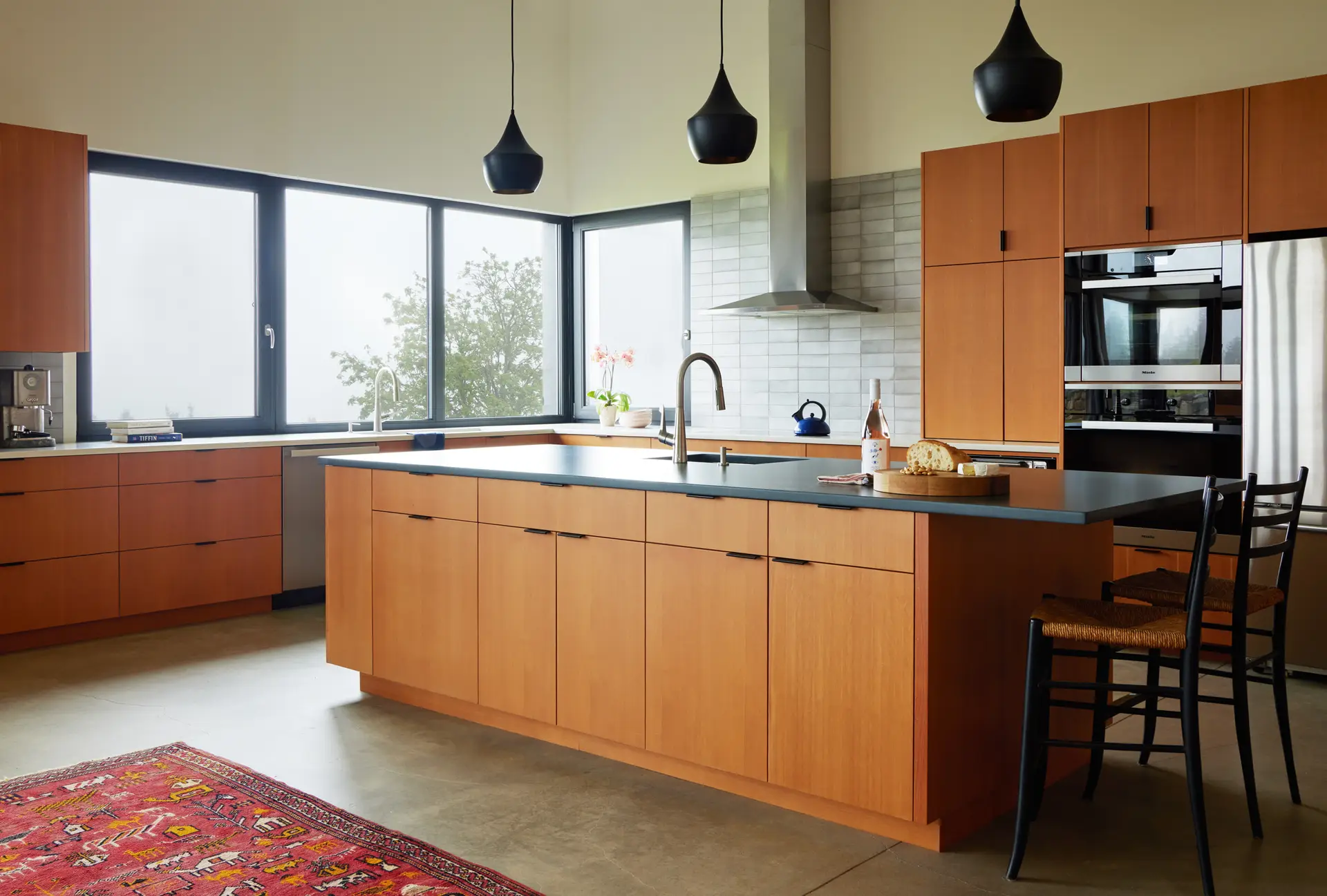 Looking at the kitchen with the sink and windows in front of the sink centered in the image. The island is in full view with seating on the left and a kitchen prep sink in the island. A wall oven and microve are adjacent to the refiderator on the left as well.