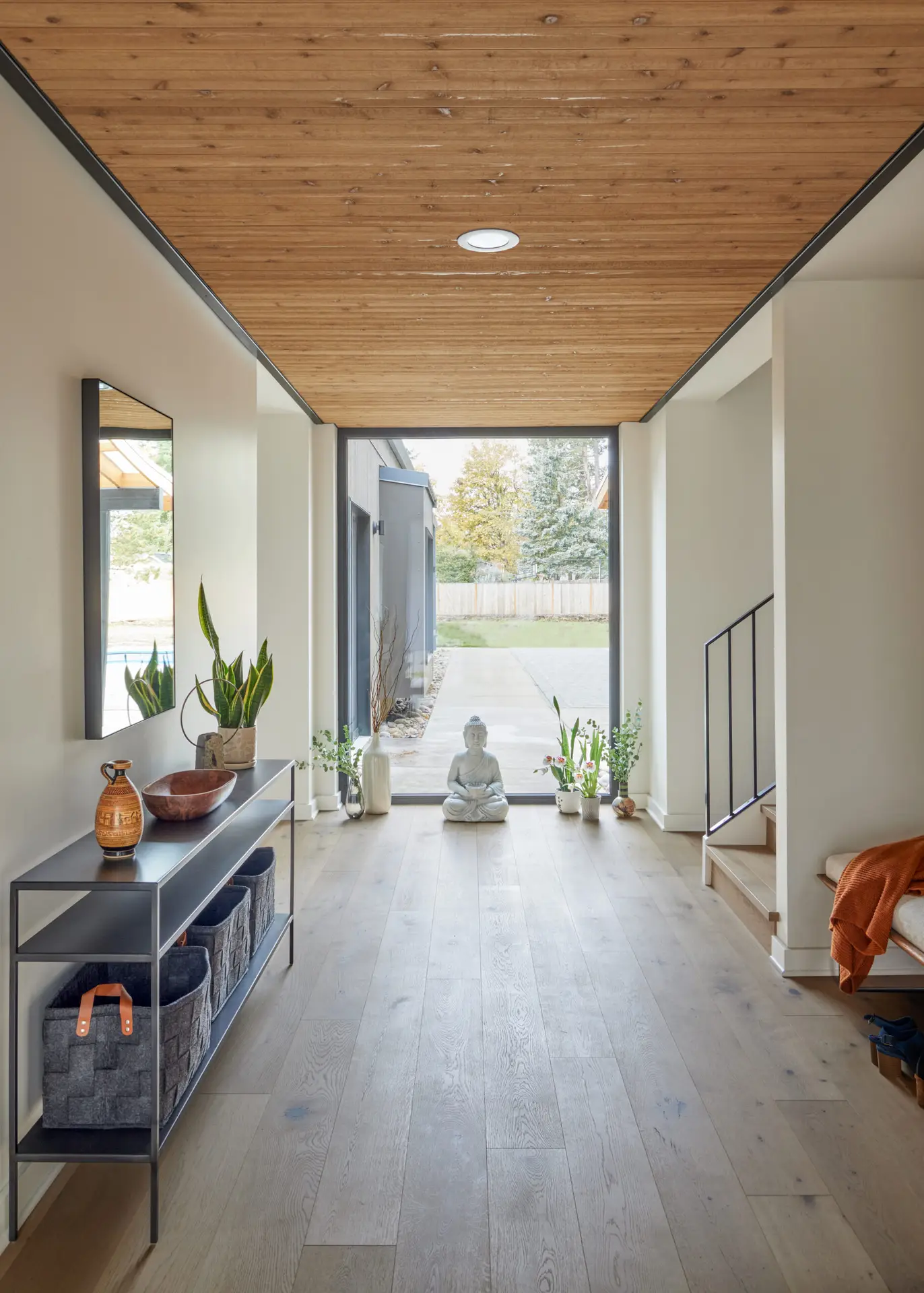 Sunset Residence foyer, featuring a large floor to ceiling window in the center of the frame with a warm wood ceiling that guides the direction toward the large window. A small statue of Buddha is on the ground and centered on the window.