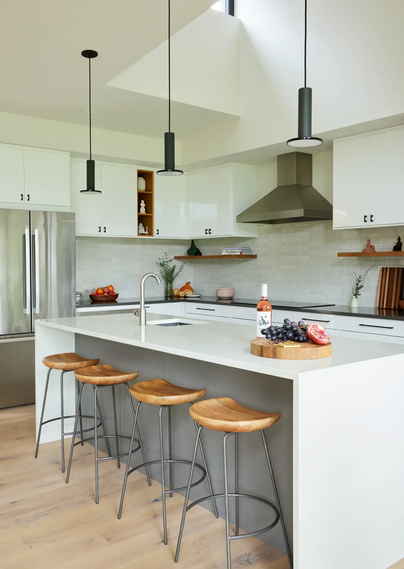 Sunset Residence kitchen, featuring a brightly rendered space with light walls and cabinets. A kitchen island with waterfall edge is the main focus on the frame with 4 counter height chairs in the foreground.