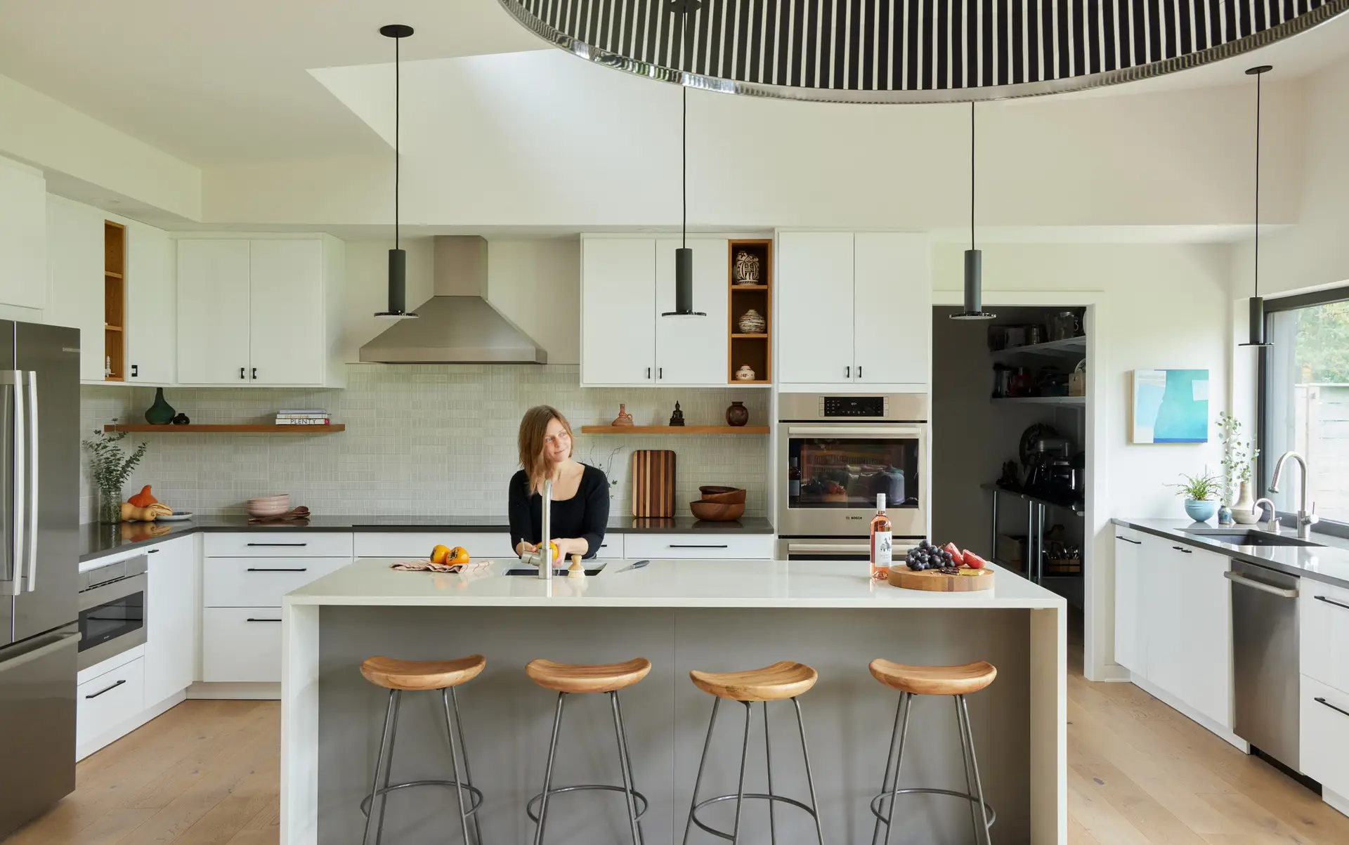 Sunset Residence kitchen, featuring a brightly rendered space with light walls and cabinets. A kitchen island with waterfall edge is centered on the frame with 4 counter height chairs.