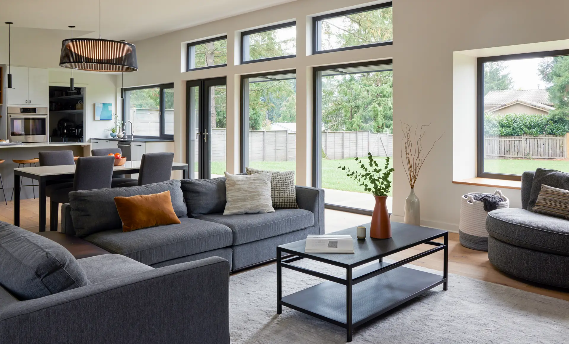 Sunset Residence living room, highlighting the open concept living/dining/kitchen setup as well as many windows that march along the exterior wall, including 3 clerestory windows.