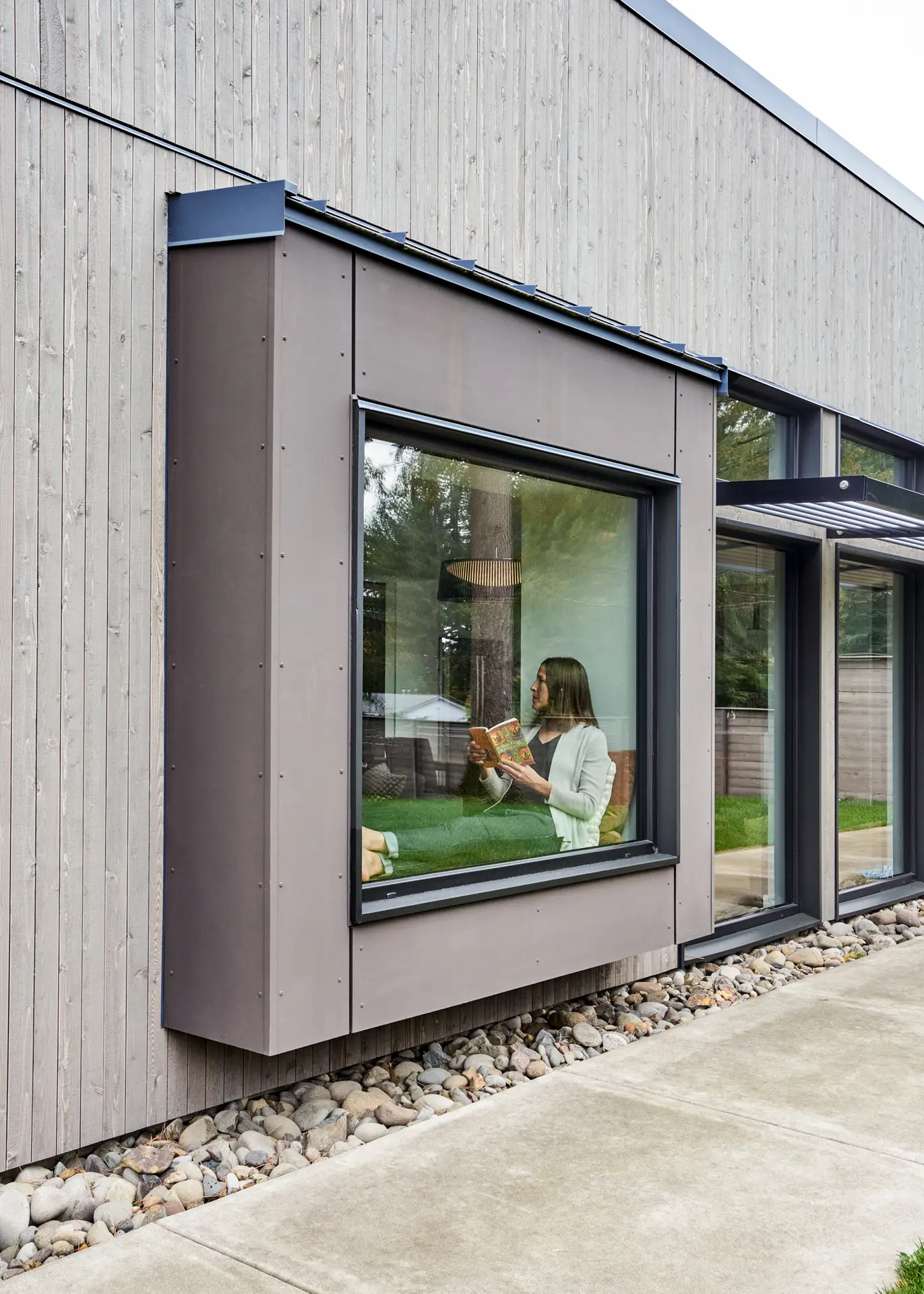 Sunset Residence exterior view, featuring the built in window seat that can be seen extruding from the primary building to allow for the interior space to sit. The siding is a combination of cool grey wood and fiber cement siding.