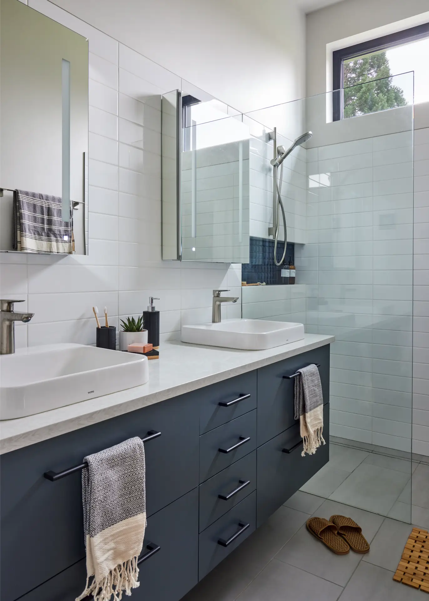 Sunset Residence bathroom, featuring a double vanity with dark blue cabinets and 2 medicine cabinets above.