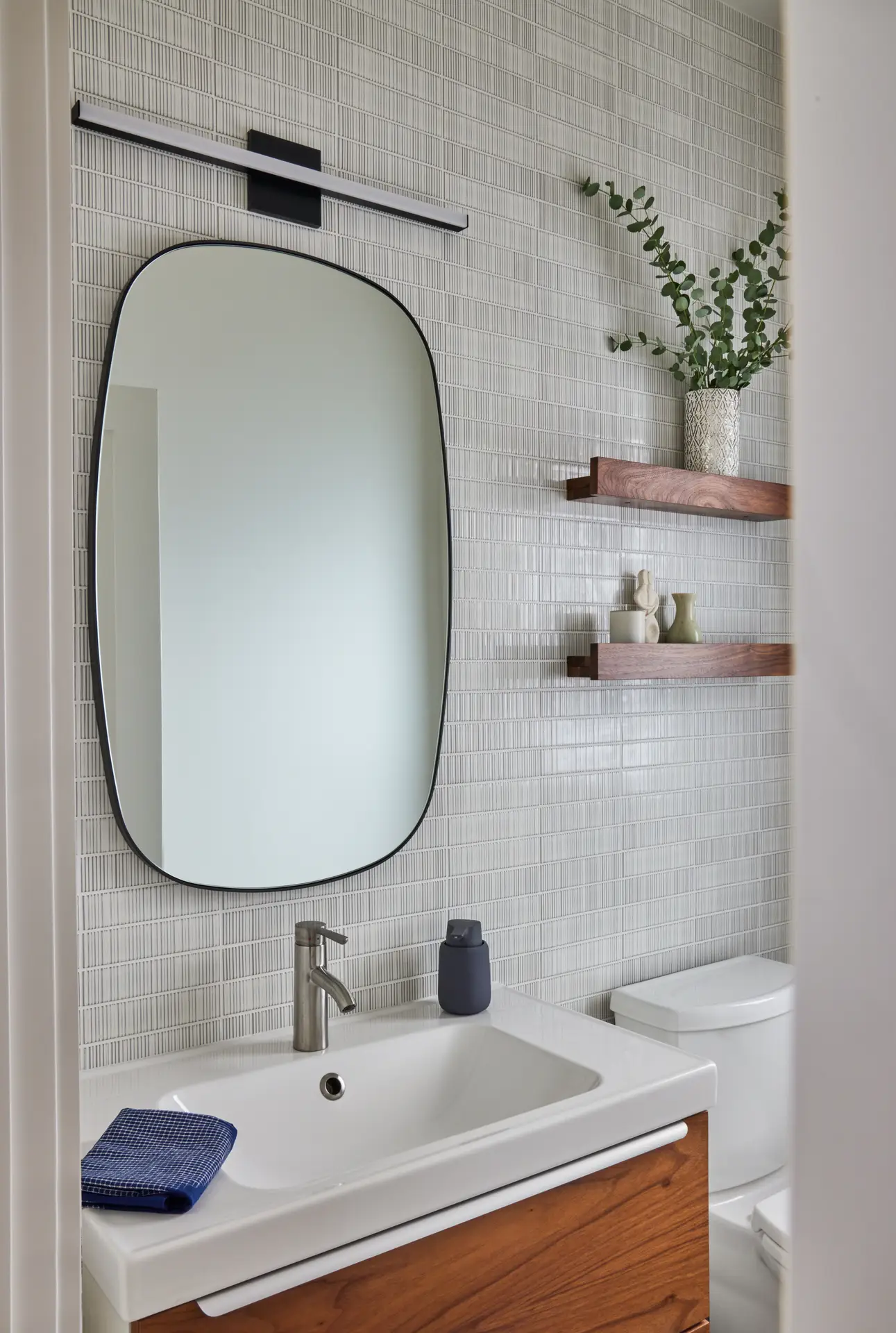 Sunset Residence bathroom, featuring a warm wood vanity and rounded rectangle mirror.