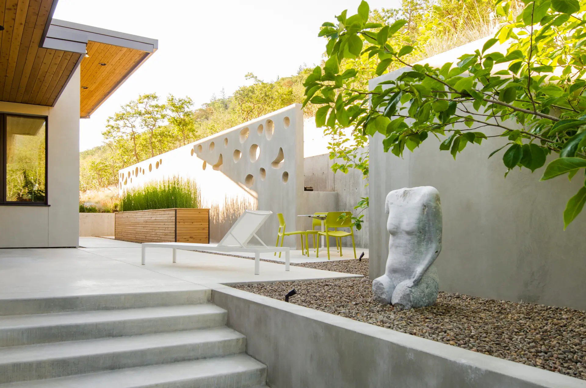 Fineline Custom Home courtyard. A minimalist courtyard with a custom perforated concrete wall with varied-sized cutouts. The landscape is finished with concrete paving, pea gravel and a large white torso sculpture.