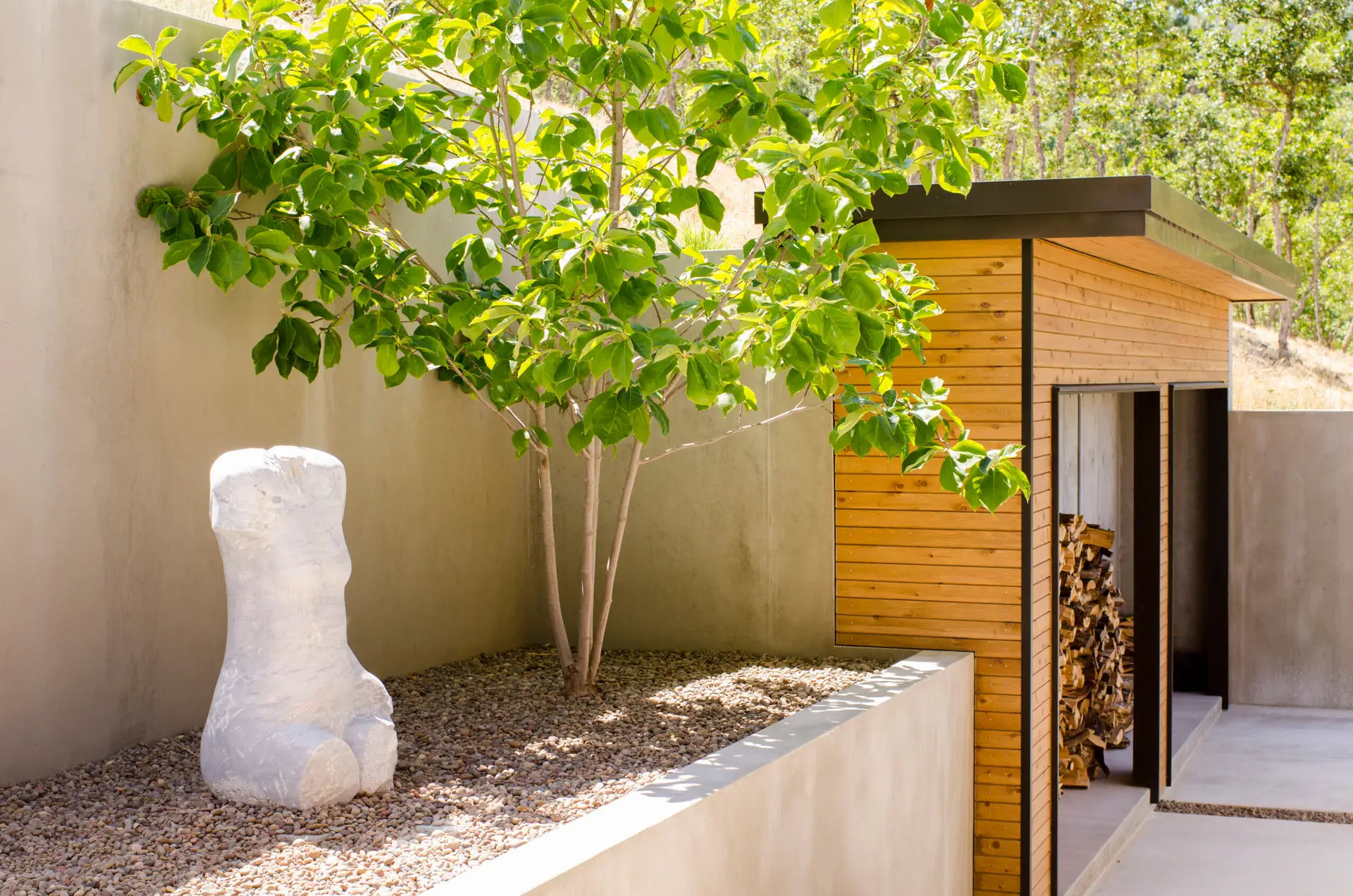 Fineline Custom Home courtyard. A minimalist courtyard with a custom perforated concrete wall with varied-sized cutouts. The landscape is finished with concrete paving, pea gravel and a large white torso sculpture.