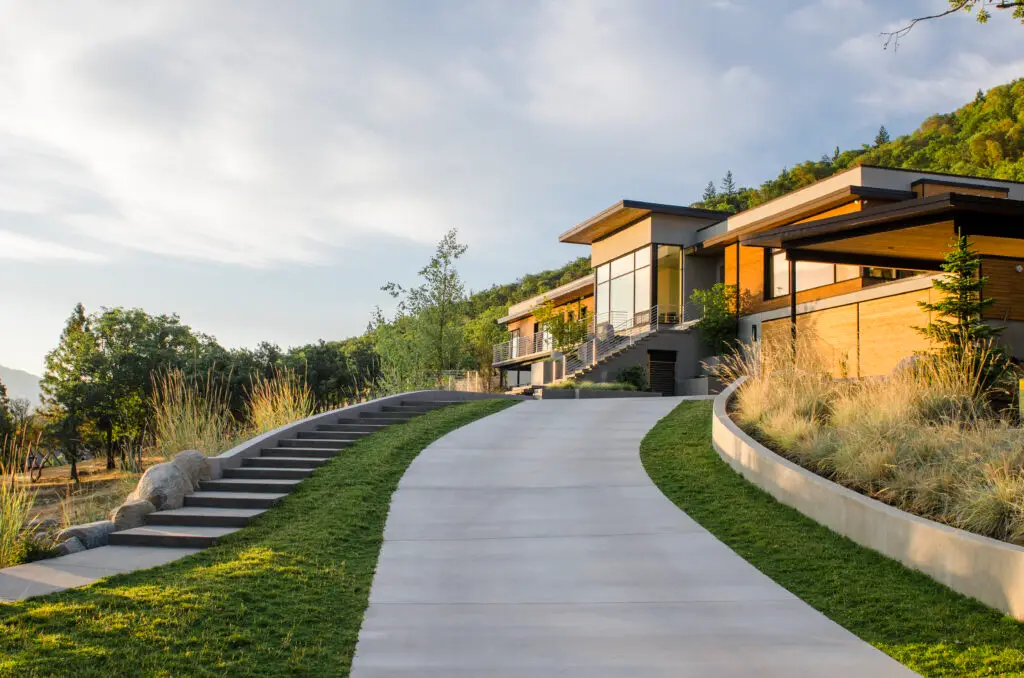 Fineline Custom Home as viewed from the end of the driveway during sunset. The home is built into a steeply sloping, north-facing hillside, utilizing a terraced design to minimize site disturbance and maximize the dramatic views of the surrounding valley.