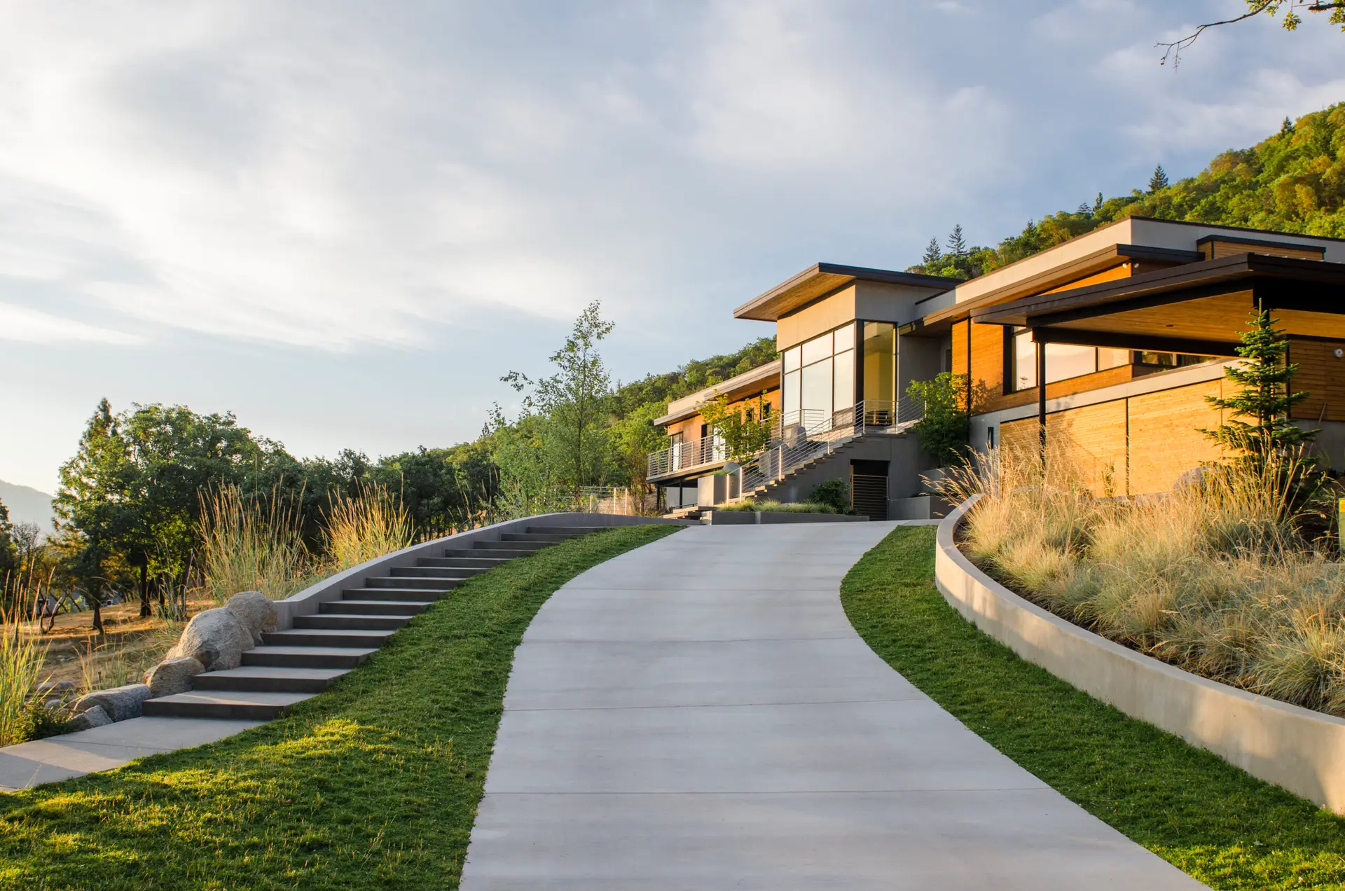 Fineline Custom Home as viewed from the end of the driveway during sunset. The home is built into a steeply sloping, north-facing hillside, utilizing a terraced design to minimize site disturbance and maximize the dramatic views of the surrounding valley.