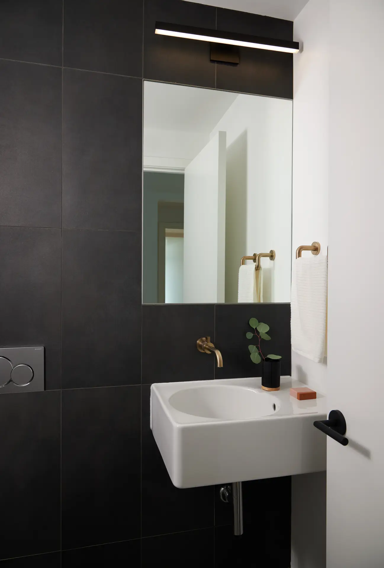 The powder room wall mounted sink with a single-handle brushed-gold wall-mounted faucet is paired with a matching gold towel ring, adding a touch of refined warmth to the monochromatic palette.