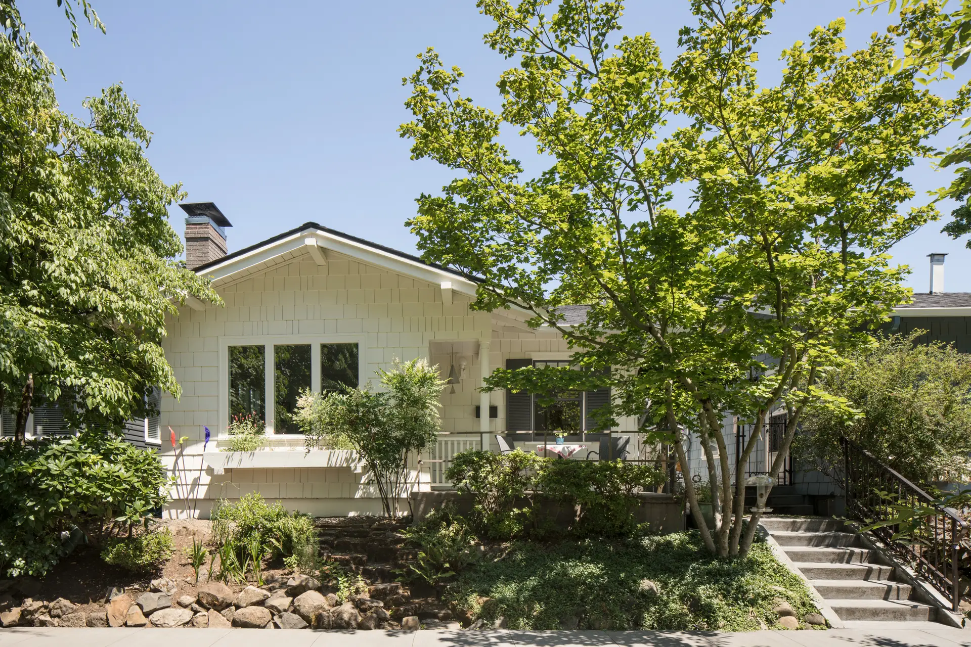 Little Larch Renovation street view, highlighting a charming bright white craftsman style home set amongst a mature, sloped landscape.