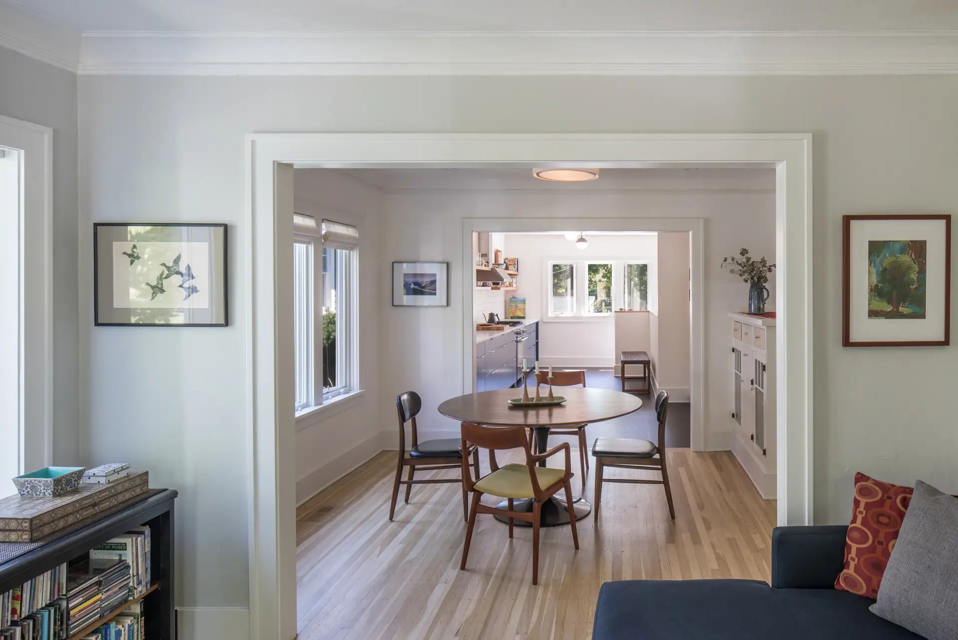 Little Larch dining room. The image is framed by an opening between the living space and the dining space. Warm wood floors run parallel with the direction of view. An additional open passage can be seen in the distance that leads into the kitchen.