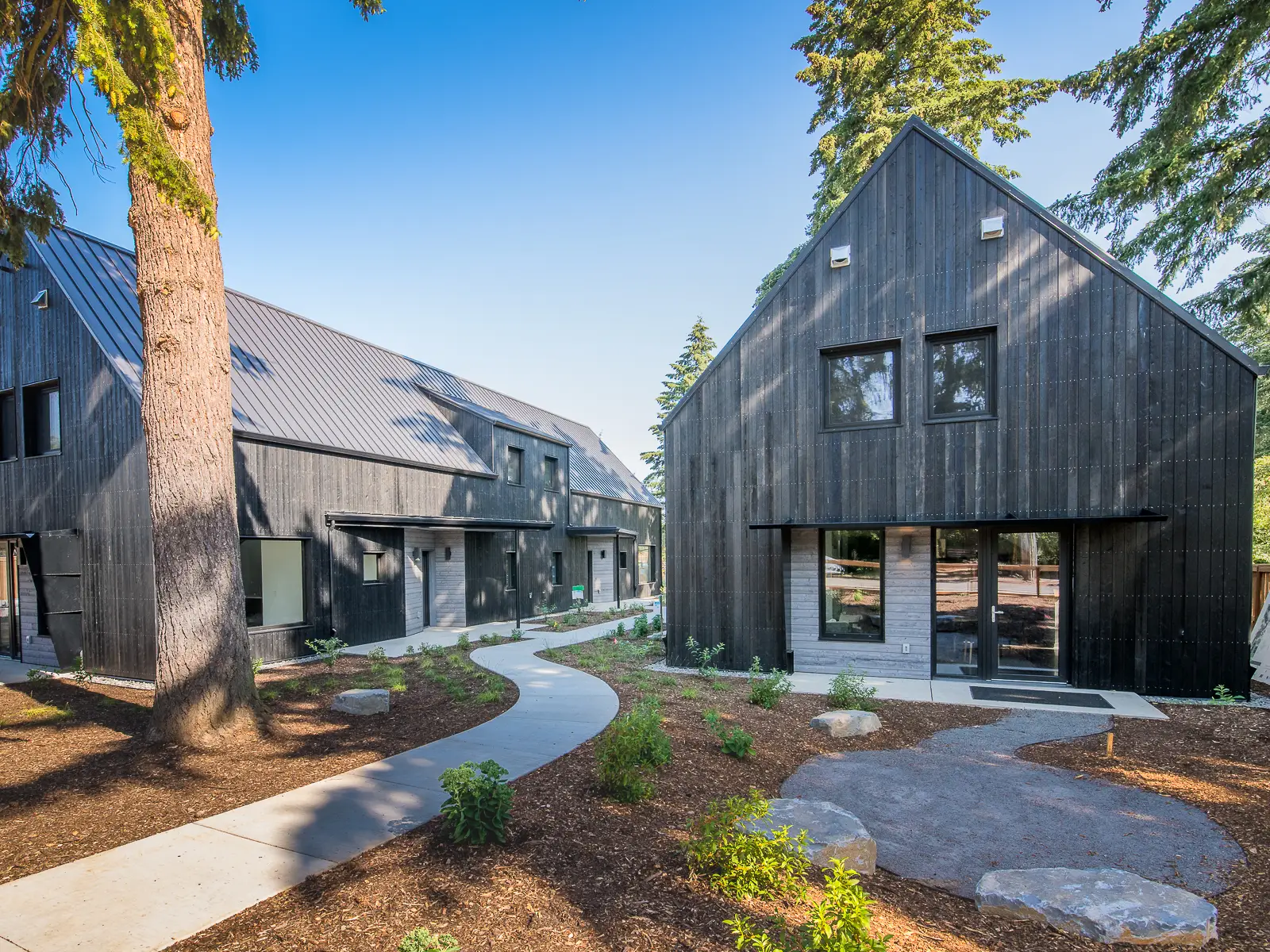 A view from Going Street showing three of the 11-unit net-zero energy homes. The buildings are a simple gable form with no overhangs and darkly stained vertical siding.