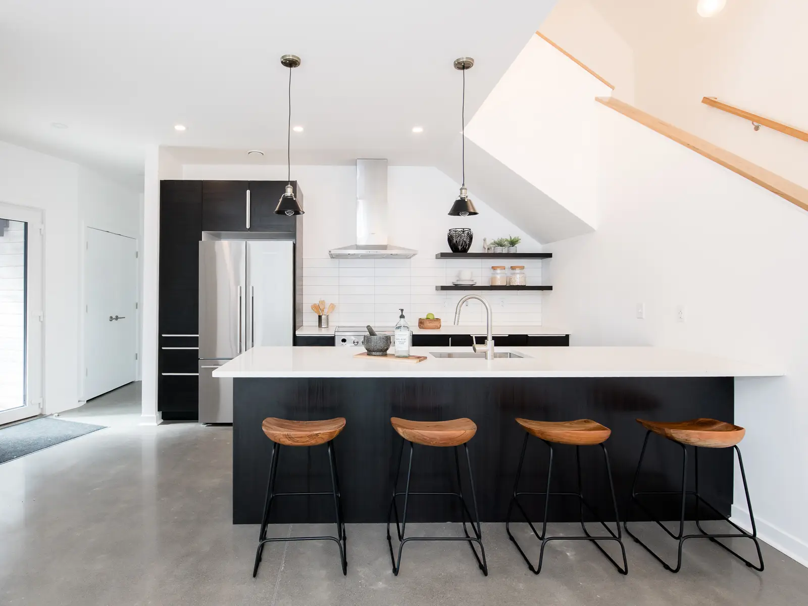 Island seating with a long white waterfall-edge serves as the central hub, providing a large workspace and seating for four. It is paired with sculpted wood bar stools with black metal legs, which add organic warmth to the industrial space.
