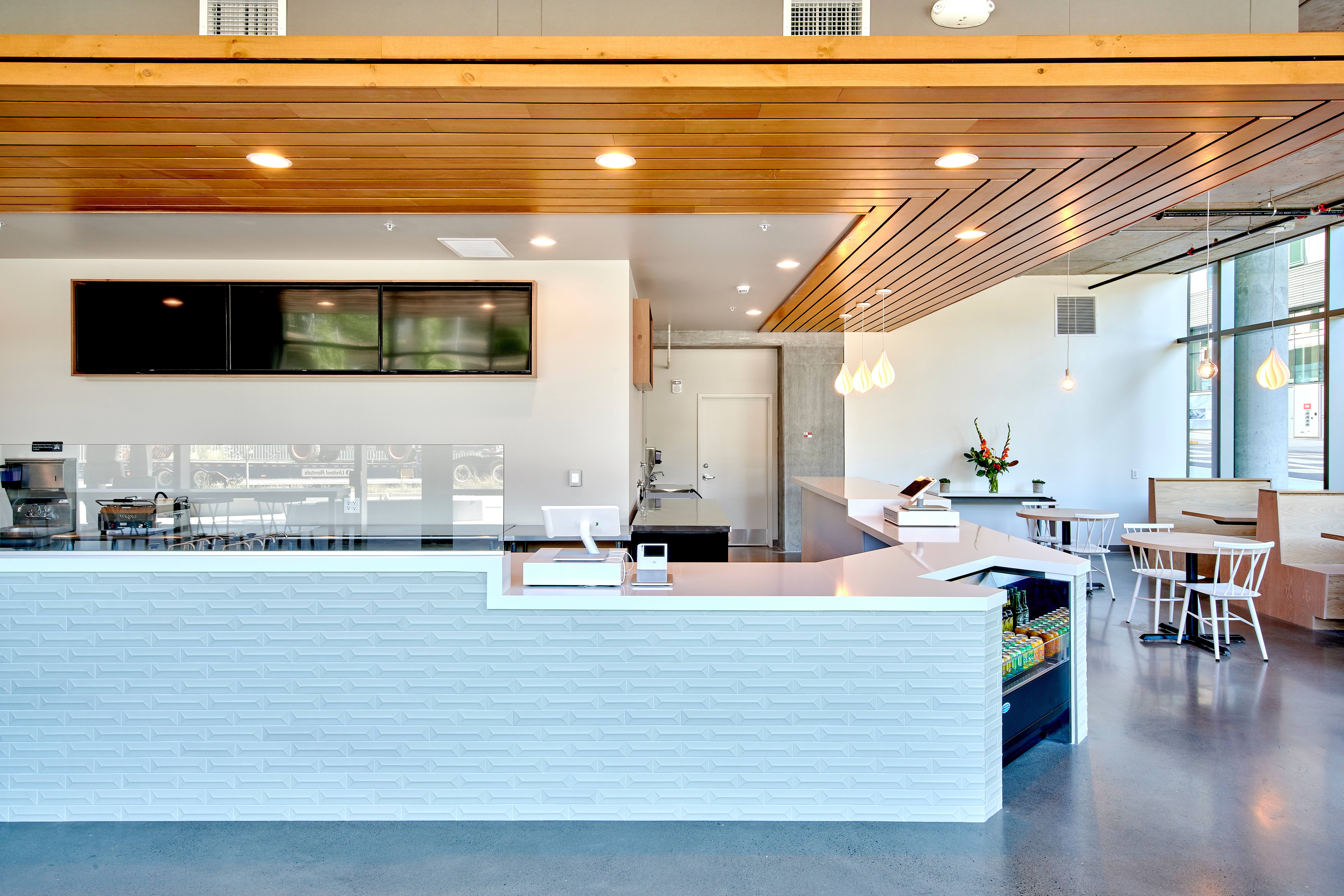 Counter at Olia Poke, featuring a tile faced lower with white countertop as well as a warm wooden dropped ceiling that follows the footprint of the counter.