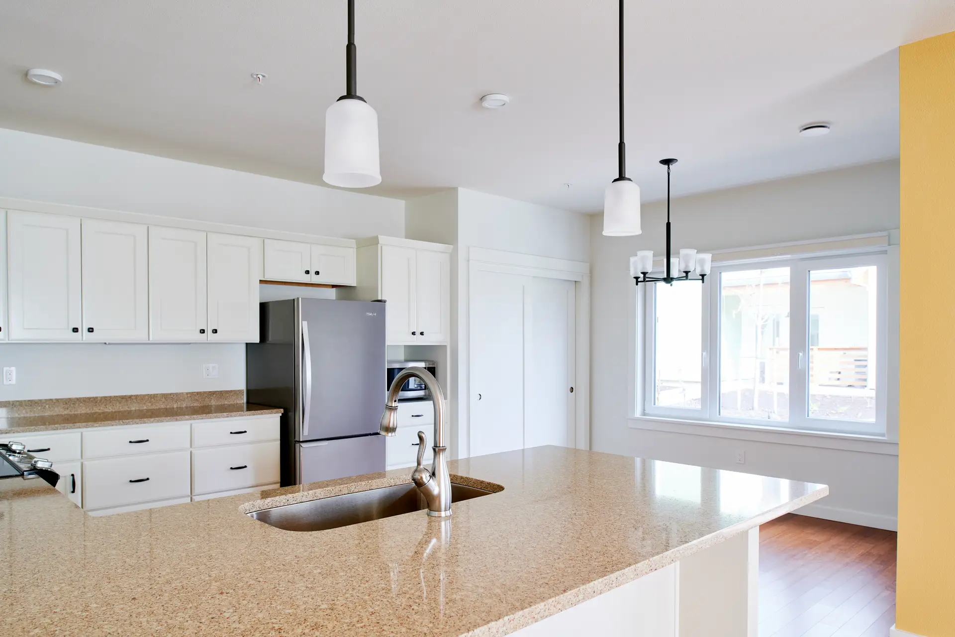 The Oaks at Rose Villa kitchen, showing a tan countertop island and light and bright cabinets and walls. Light is filling the space from a large window at the back of the frame.