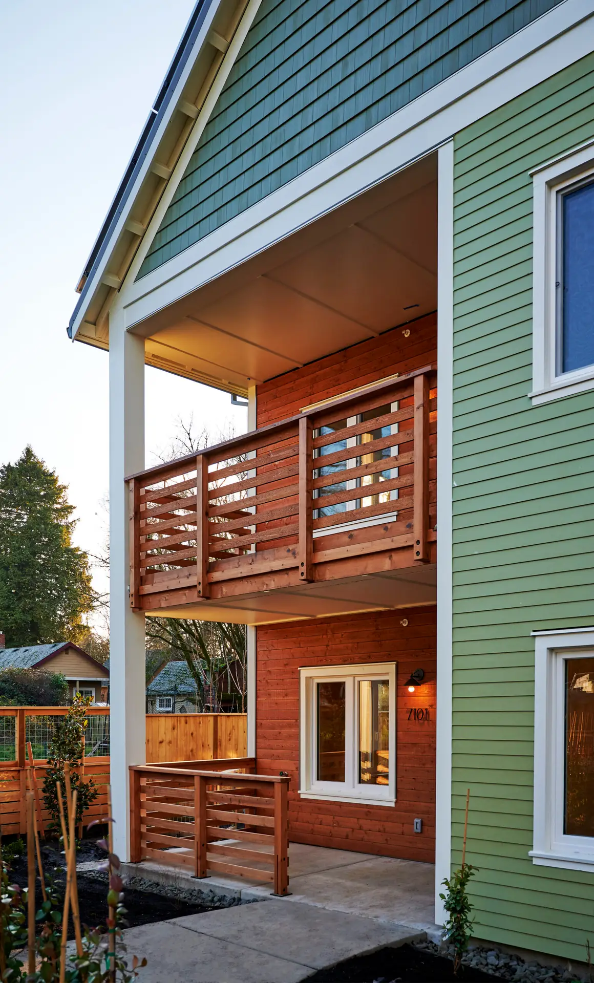 The Oaks at Rose Villa from the exterior. The building reflects the craftsman style of the neighborhood and features light green horizontal cladding combined with slightly darker green shake siding at the gable end. There are also set back porches that feature warm wood cladding.