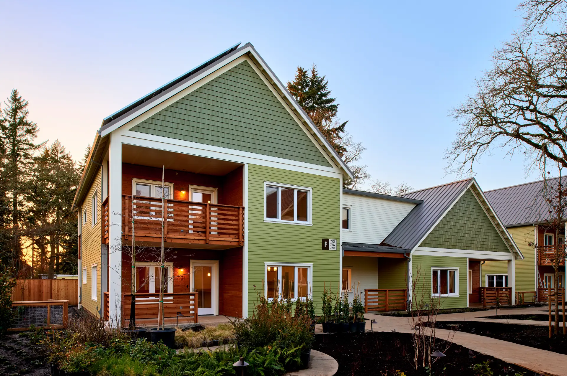 The Oaks at Rose Villa from the exterior. The building reflects the craftsman style of the neighborhood and features light green horizontal cladding combined with slightly darker green shake siding at the gable end. There are also set back porches that feature warm wood cladding.