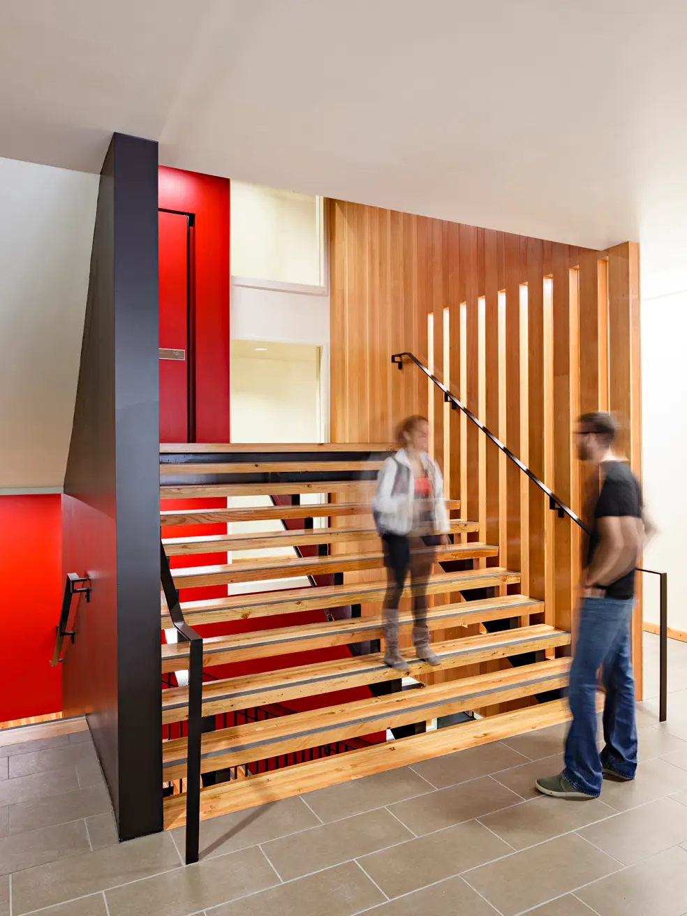 Lewis and Clark college, showin an open riser stair that is generously sized for high traffic. The wood tones invite users up the stairs with both the treads and slat rail.