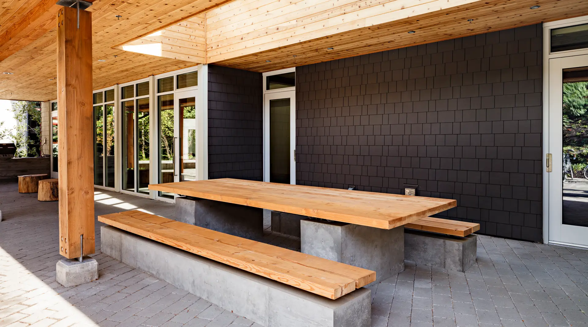 Lewis and Clark college, showing a detail view of a built in bench and table that is constructed of a wood board on top of a concrete plinth. The design showcases a commitment to sustainability by reusing approximately 75% of the big-leaf maple and Douglas fir trees that were originally felled on-site during construction. These trees were transformed into functional and decorative elements, including tables, benches, and this unique focal wall.