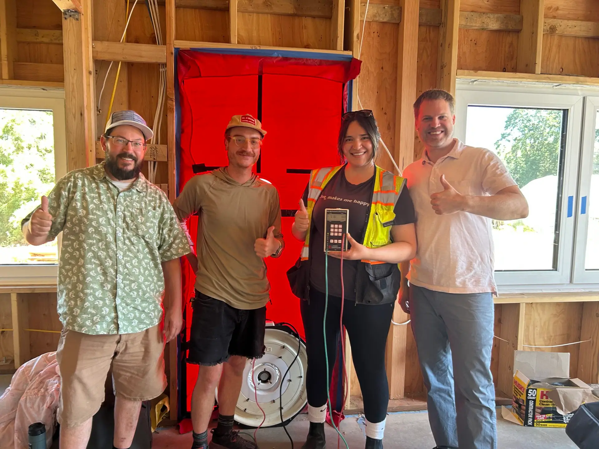 The Green Hammer project team standing infront of the blower door test setup, celebrating a low blower door score.