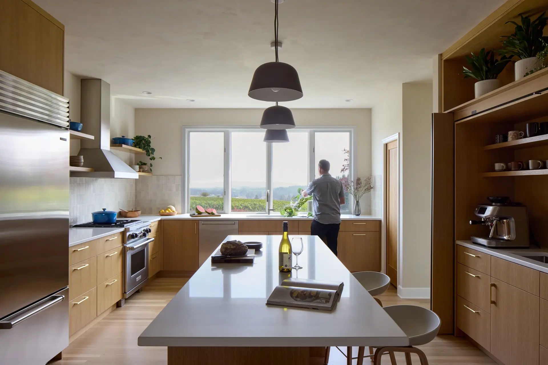 Overview of the kitchen with the island as the focal point and expansive windows in the background looking out towards the vinyard. On the rignt is the coffee bar and on the left is the range and sub-zero refridgerator.