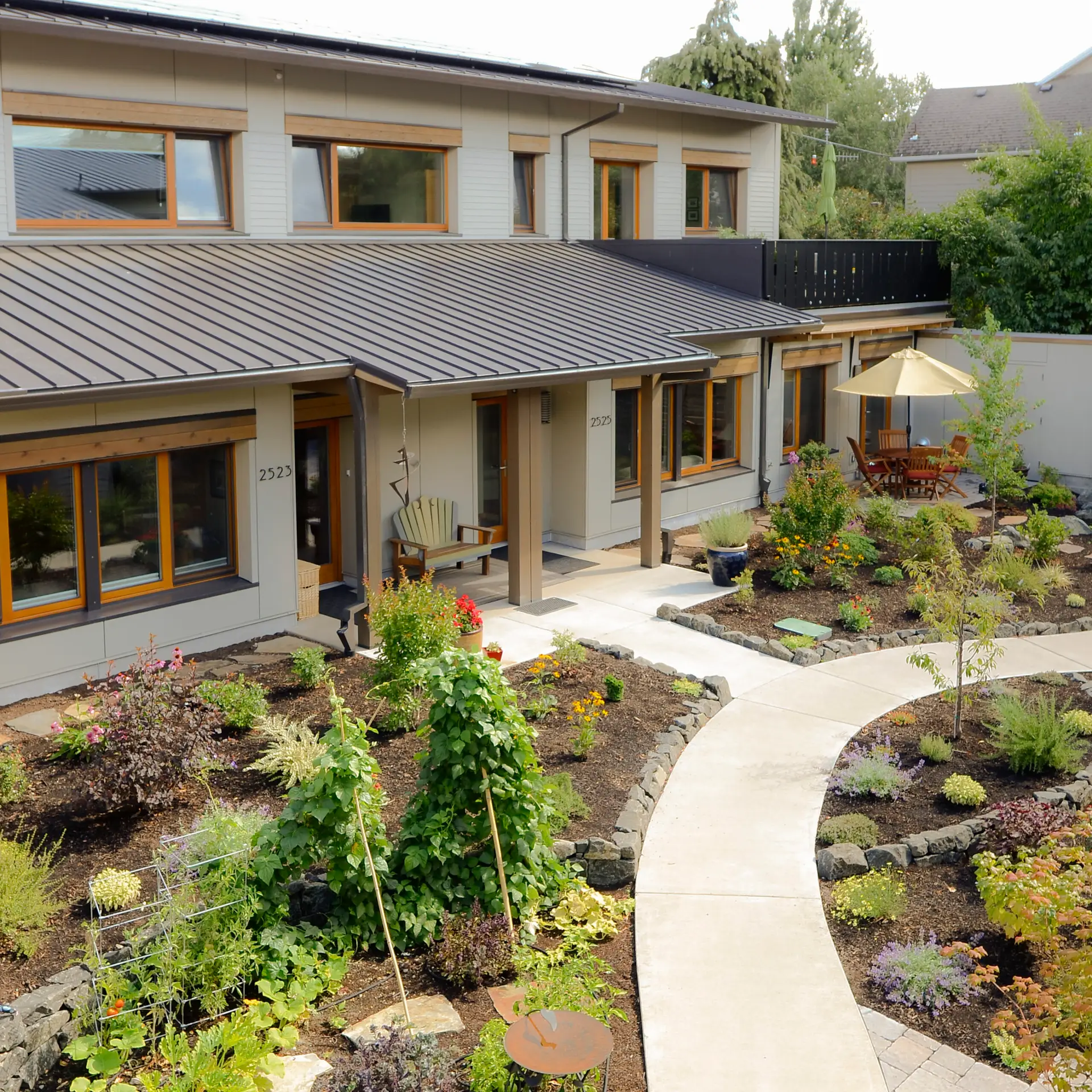 Ankeny Row exterior aerial view, showing an exterior courtyard with lush landscaping. The building features wood frame windows and a warm neutral stucco exterior