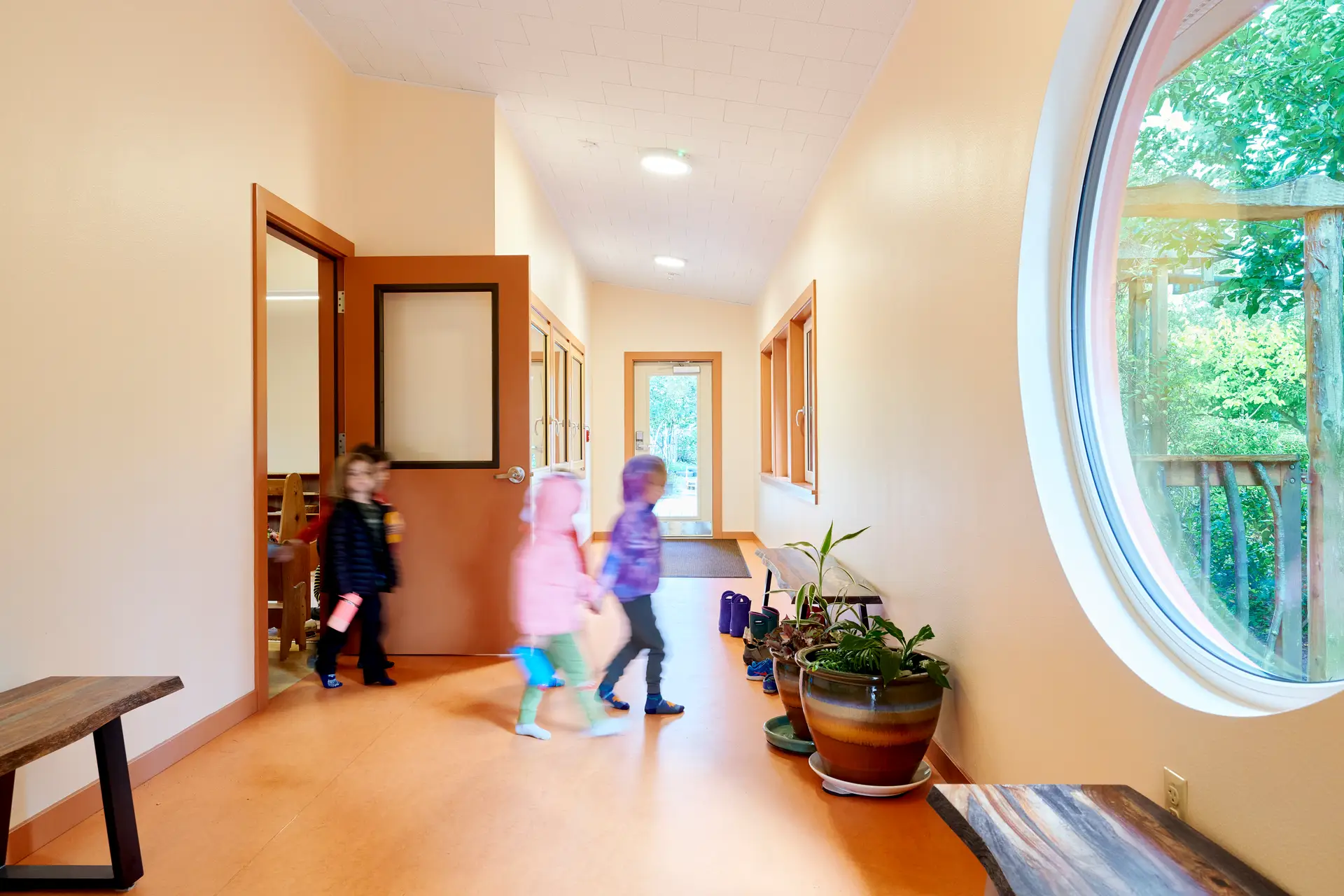 Children at New Day school walking from a classroom into the hallway. The hallway is bright from windows along the perimeter and the floor is a soft and durable cork.